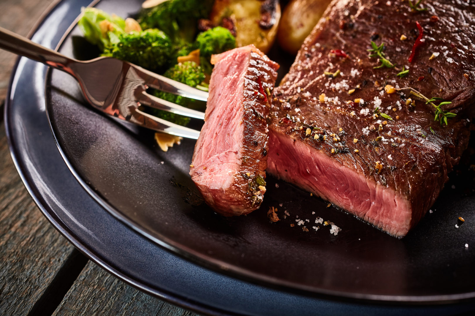 Cropped close up on cut of medium rare cooked beef steak on fork in plate with broccoli
